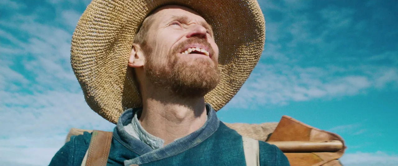 At Eternity’s Gate (2018) movie still: closeup — A man in a rustic straw hat stands against a bright, clear blue sky. He looks upward with a smile,…