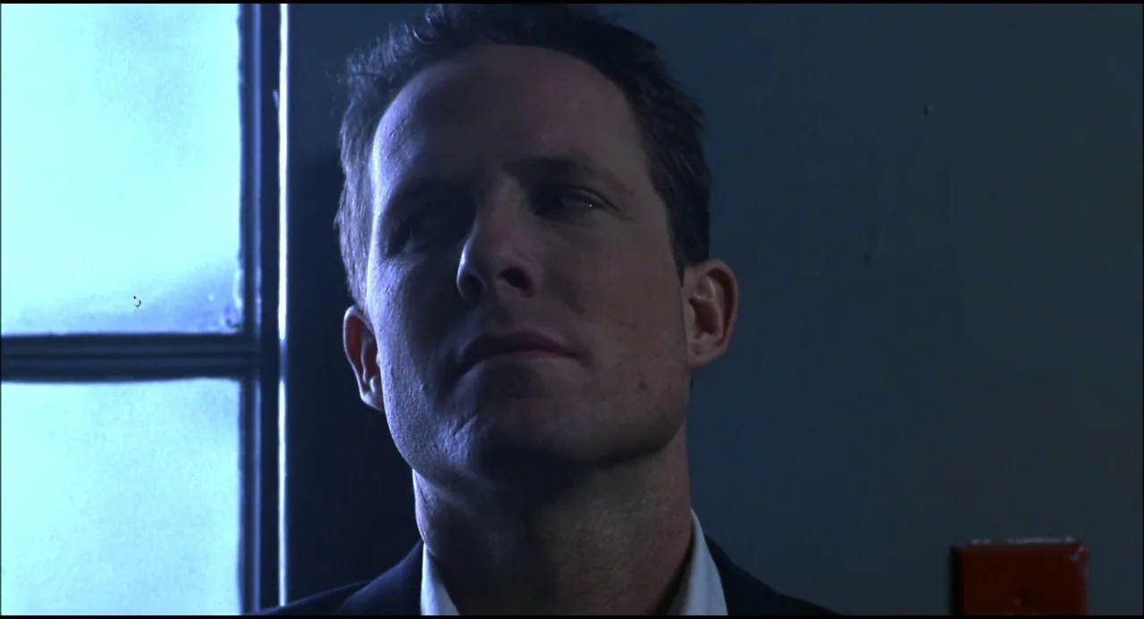 Hellraiser: Hellseeker (2002) movie still: closeup — A man stands in a dimly lit hallway next to a window with vertical bars. He looks to the side…