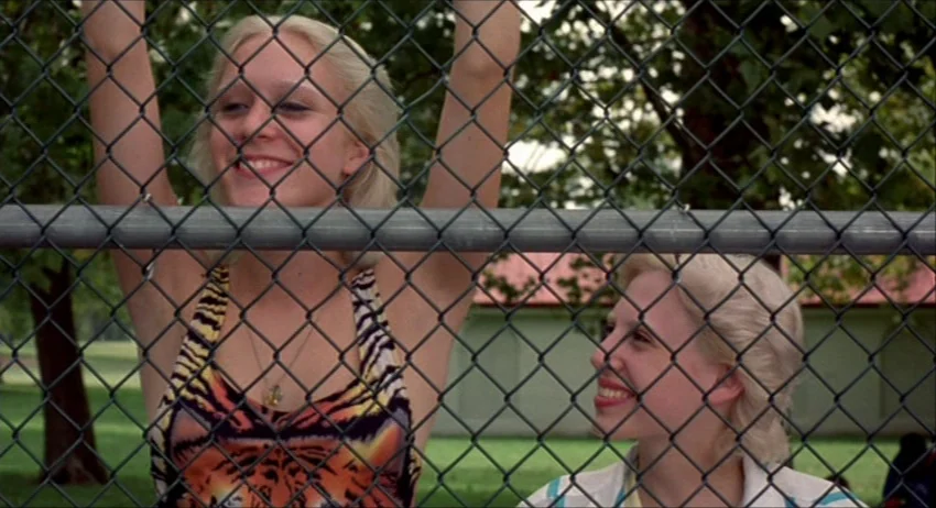 Gummo (1997) movie still: medium — Two young blonde women stand closely behind a grey metal chain link fence. They look toward each other while…