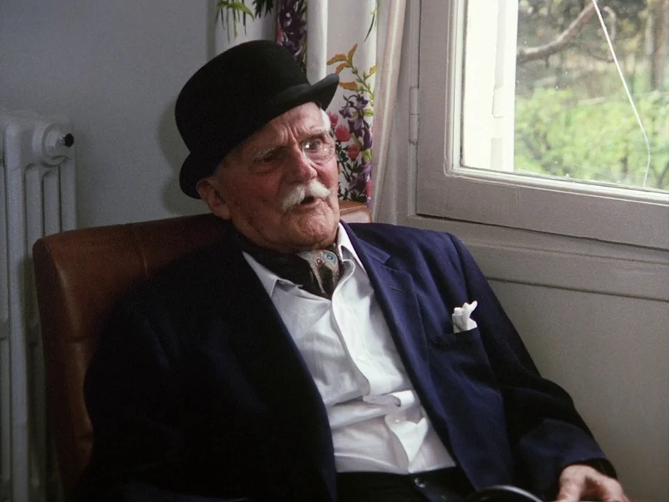 The Clowns (1970) movie still: medium — An elderly man in a formal outfit sits in a brown leather chair. He is positioned next to a window with…