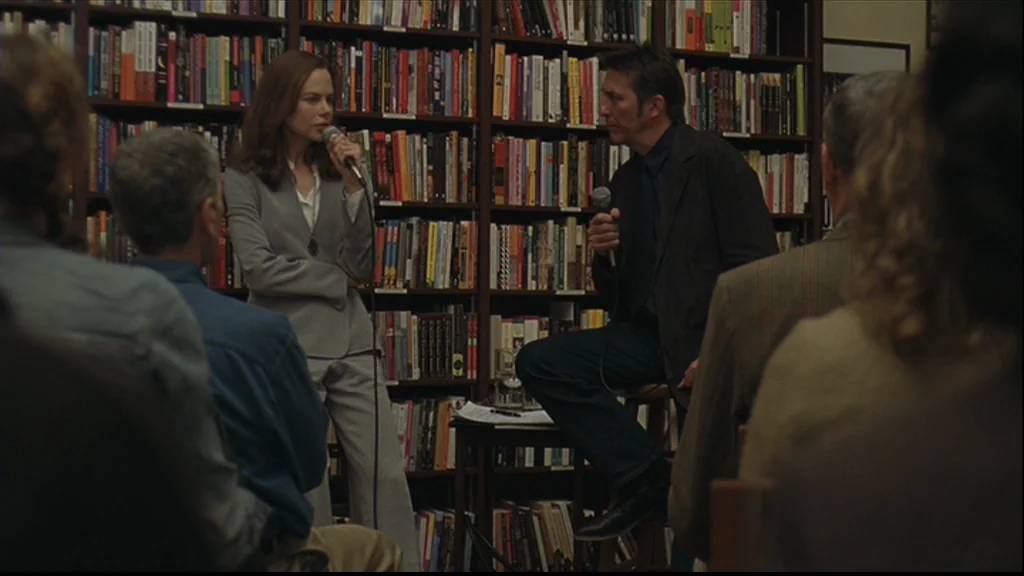 Margot At The Wedding (2007) movie still: medium — Two individuals participate in a book discussion in front of a dense bookshelf display. A woman…