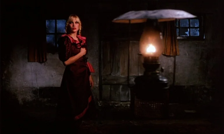 Katie Tippel (1975) movie still: medium — A dark, dimly lit room has rough textured walls and small, paned windows. A woman wearing a dark red dress…