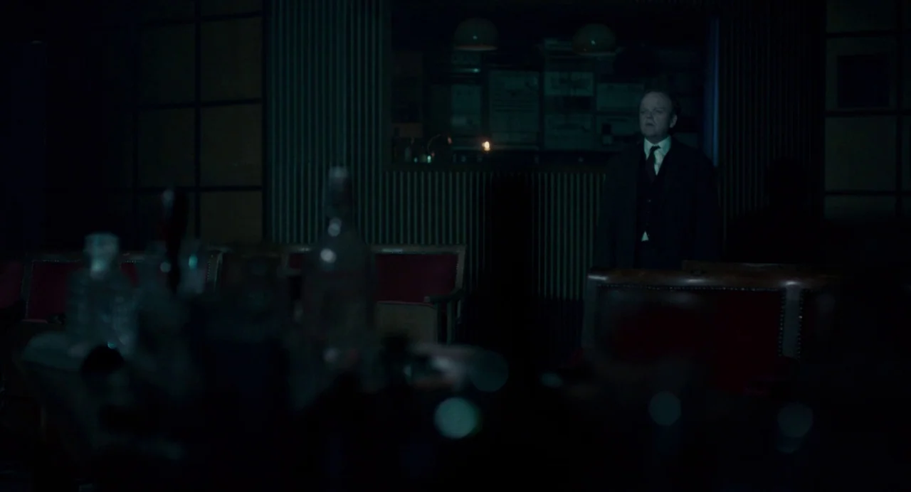 Berberian Sound Studio (2012) movie still: medium — A dimly lit room features red padded seating and textured dark wall paneling. A middle-aged man…