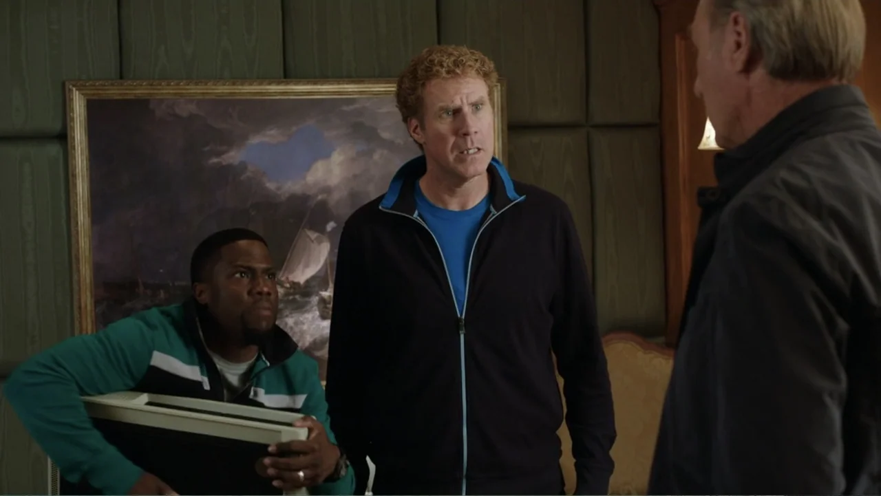Get Hard (2015) movie still: medium — An interior space features olive-green padded wall panels and a large framed painting. Two men stand in the…