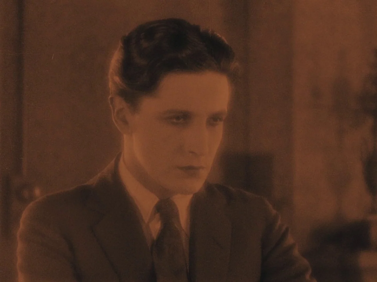 The Lodger (1927) movie still: medium — A man stands in a dimly lit room with simple wall decor. He maintains a steady gaze while facing slightly…