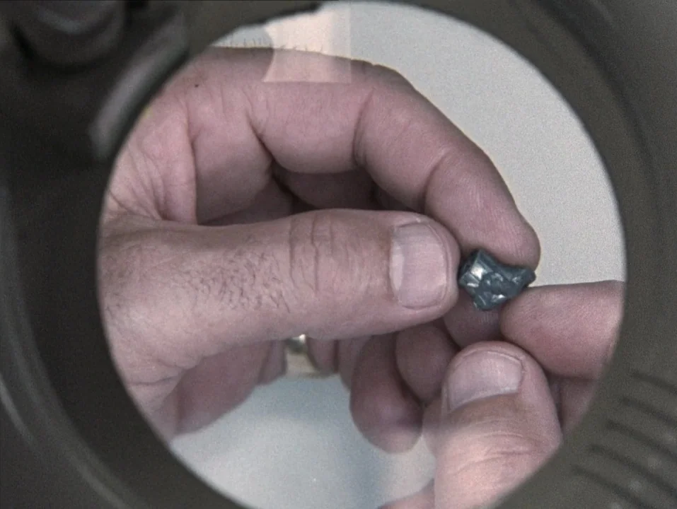 River of Grass (1994) movie still: closeup — A view through a circular magnifying glass shows hands holding a small, metallic object. The background…