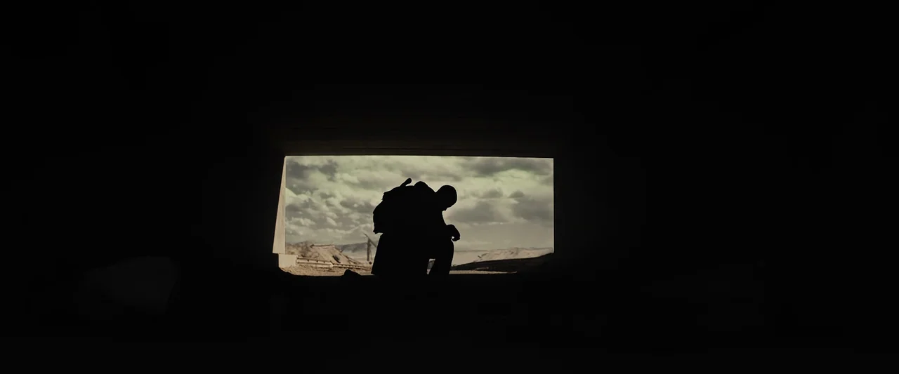 The Book of Eli (2010) movie still: wide — A dark concrete tunnel frame looks out onto a desolate, cloudy, arid desert landscape. A lone person…