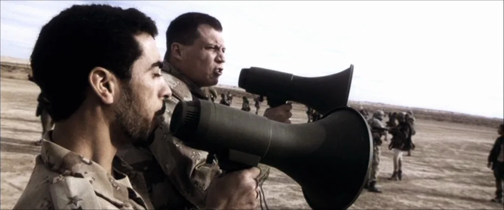 Three Kings (1999) movie still: medium — An open desert landscape with a group of soldiers standing in the distance. Two men in military uniforms…