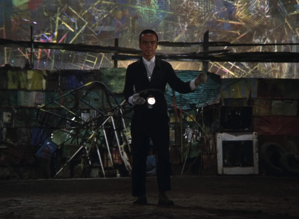 Dodes’ka-den (1970) movie still: fullbody — A vast collection of discarded metal objects and tires forms a cluttered perimeter. A man in dark…