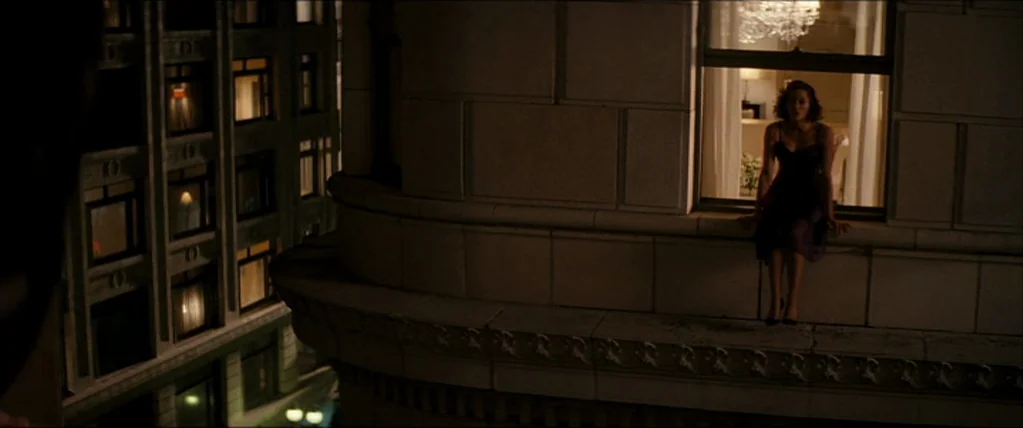 Inception (2010) movie still: wide — A woman sits on the stone ledge of a tall building at night. She is positioned next to an open window that…
