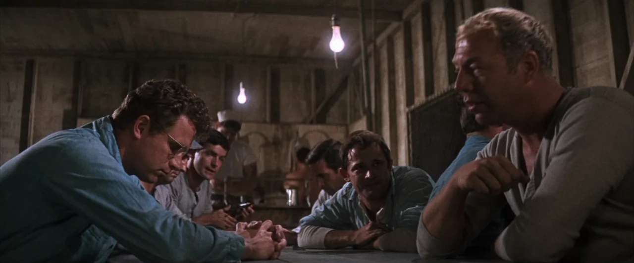 Cool Hand Luke (1967) movie still: medium — A rustic wooden barracks features bare light bulbs hanging from exposed ceiling beams. A group of men in…