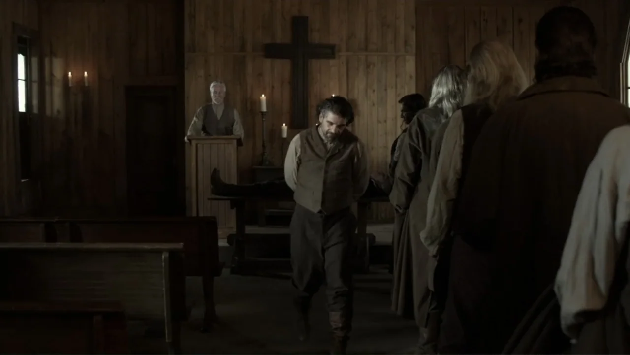 Dawn Rider (2012) movie still: medium — A wooden church interior features a large wall-mounted cross behind a small pulpit. A man with his hands…