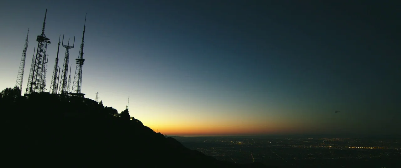 Nightcrawler (2014) movie still: establishing — A high-altitude view of a mountain ridgeline featuring several tall broadcasting communication…