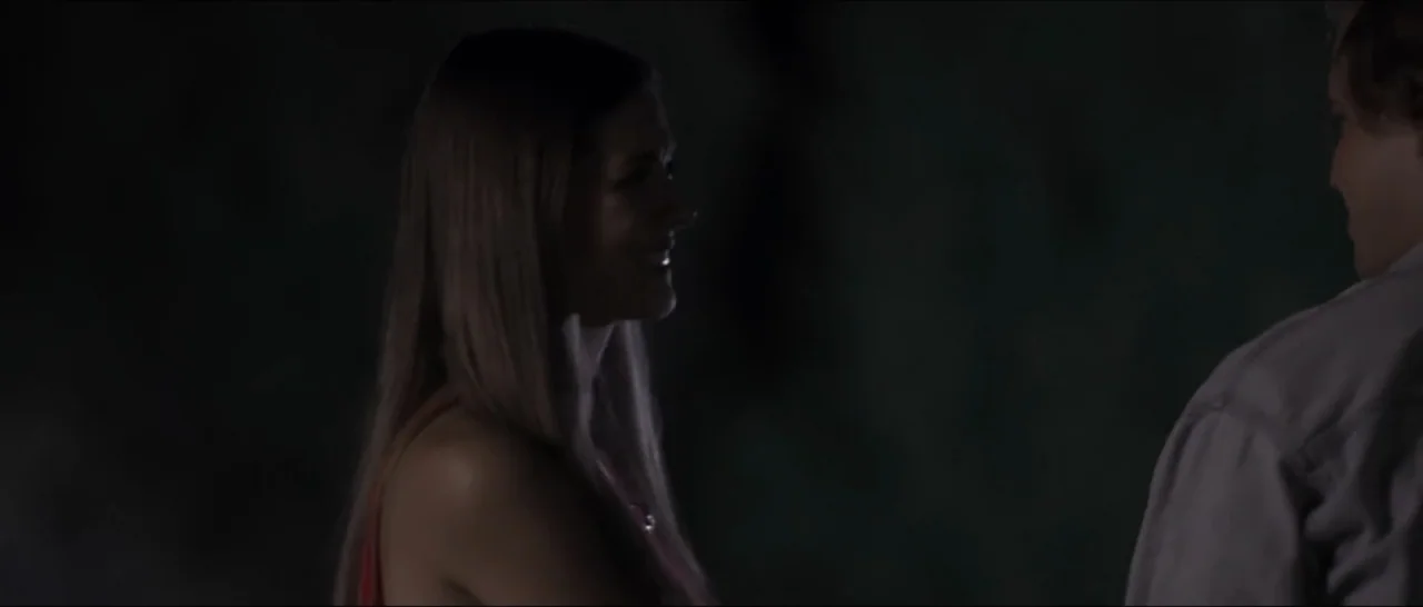 If You're Gone (2019) movie still: medium — A dark outdoor space at night with two people standing facing each other. A woman in a red top converses…