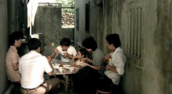 The Boys From Fengkuei (1983) movie still: wide — A narrow alleyway between concrete walls serves as a dining area for a family. Several adults and…