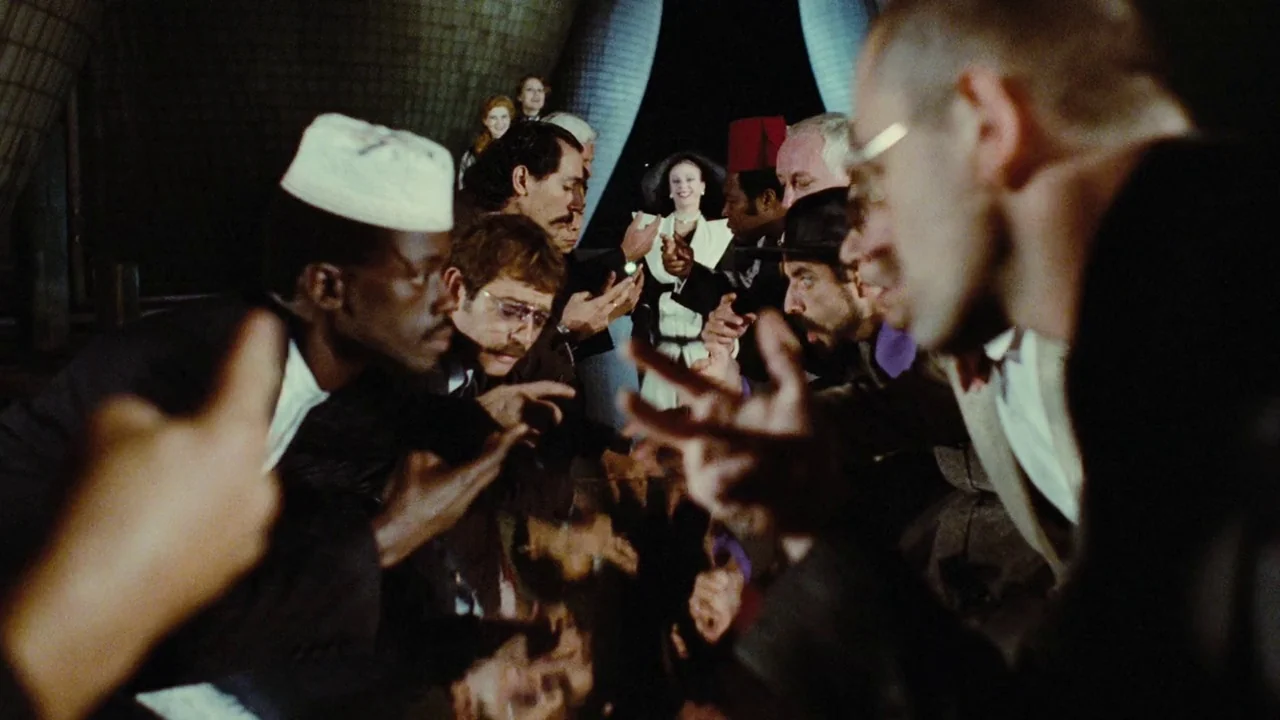 Dorian Gray in the Mirror of the Yellow Press (1984) movie still: medium — A group of formally dressed individuals gather within a dimly lit,…