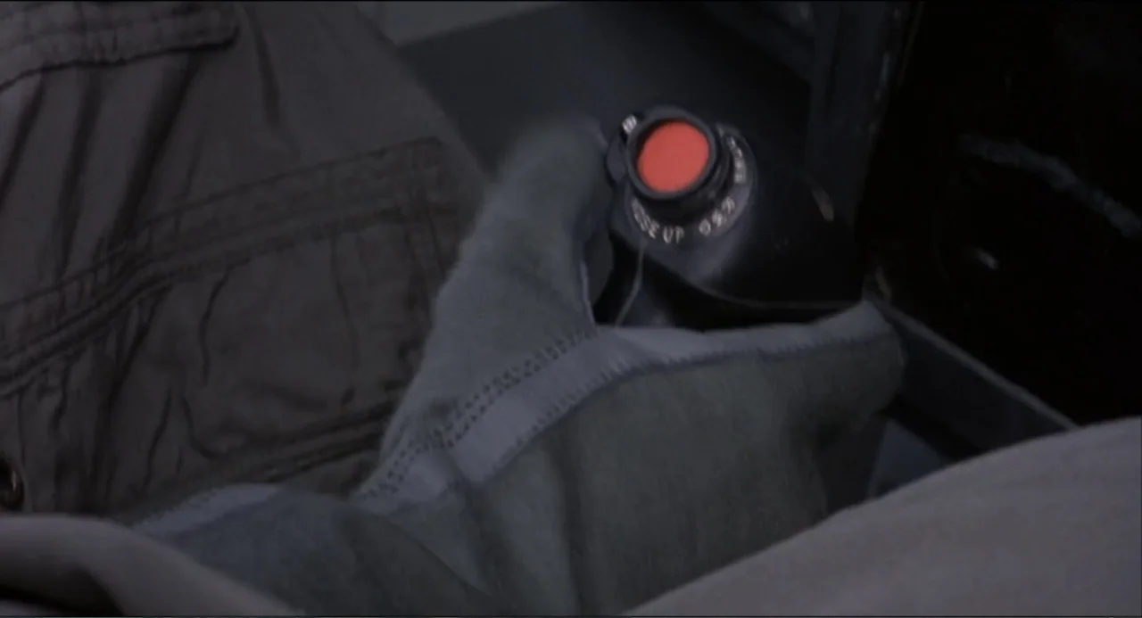 Air Rage (2001) movie still: closeup — A cramped, dark cockpit interior features military-grade flight control equipment. A gloved hand rests on a…