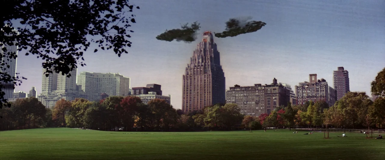 Ghostbusters (1984) movie still: establishing — A green open park field sits in front of a dense urban skyline. Two dark clouds hover symmetrically…