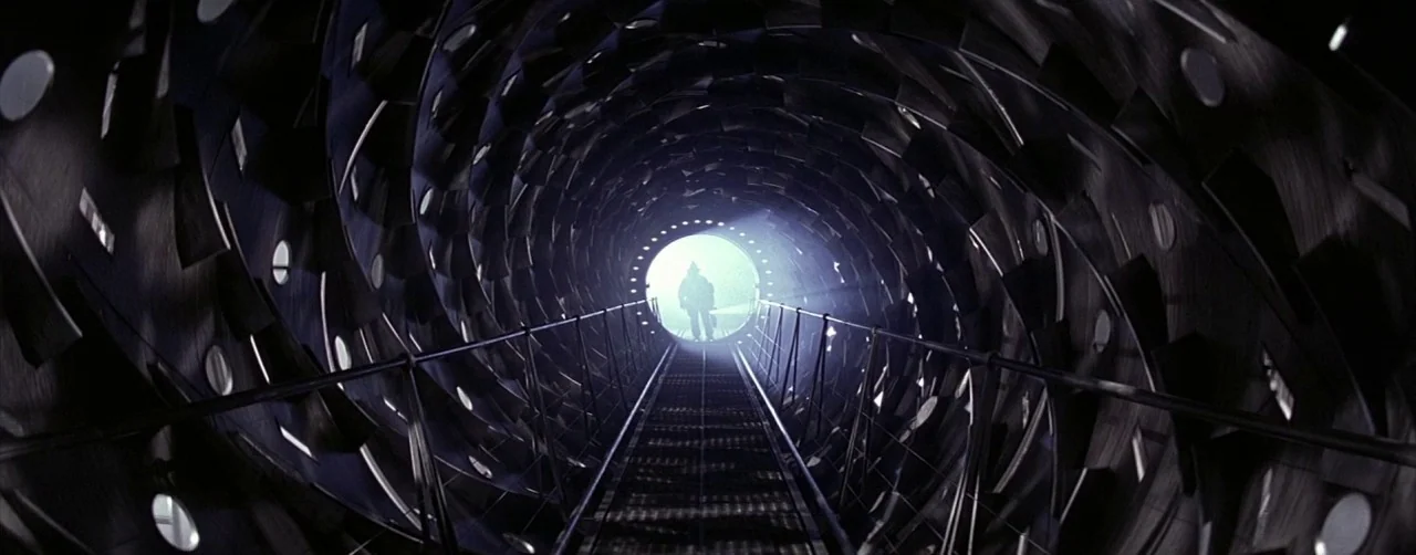 Event Horizon (1997) movie still: wide — A dark cylindrical industrial tunnel features spiraling metallic plates along its interior walls. A…