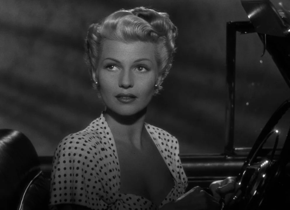 The Lady from Shanghai (1947) movie still: closeup — A woman sits behind the steering wheel of a parked convertible at night. The dark interior…