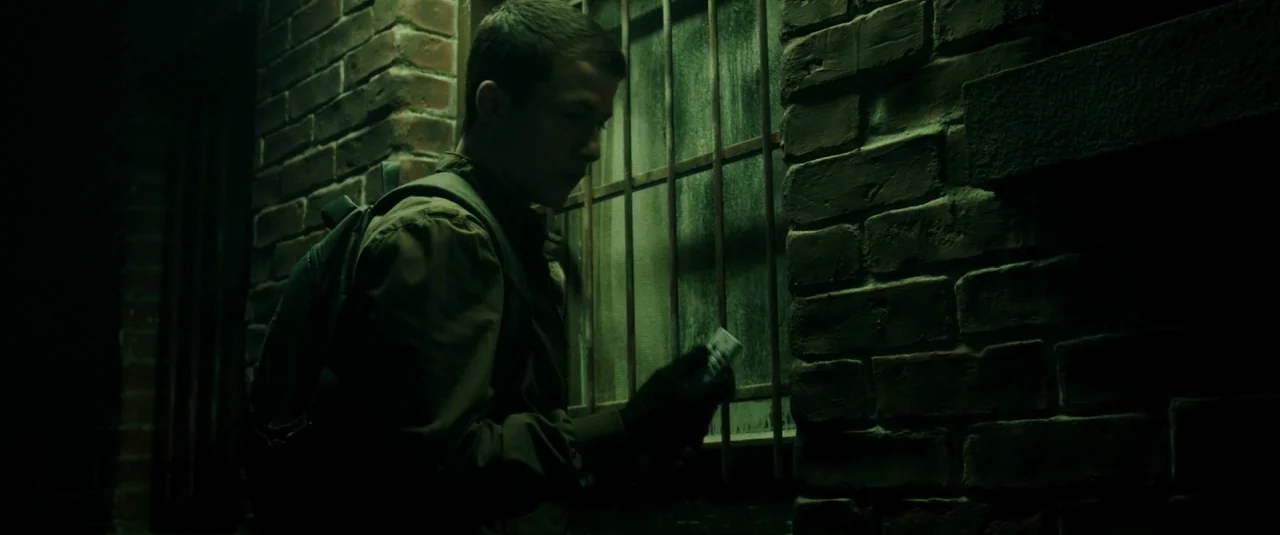 Don’t Breathe (2016) movie still: medium — A dark brick wall lines the edge of a narrow outdoor path at night. A young man wearing a jacket and…