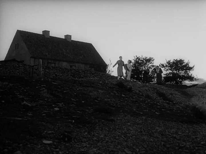 Through A Glass Darkly (1961) movie still: wide — A stone cottage stands on a desolate, rocky slope at the edge of land. Four people walk along the…