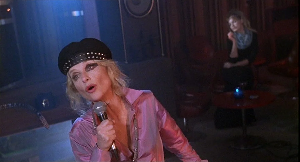 Deux (2002) movie still: medium — A dark lounge with red tables and dim, atmospheric lighting. A blonde woman performs with a microphone while a…