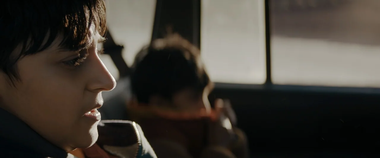 Encounter (2018) movie still: closeup — The interior of a moving vehicle shows two children sitting in the back seats. The primary child in focus…