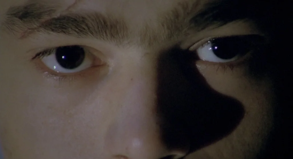 In a Glass Cage (1986) movie still: closeup — A close-up view focuses on a pair of eyes looking directly forward. Strong side lighting creates a…