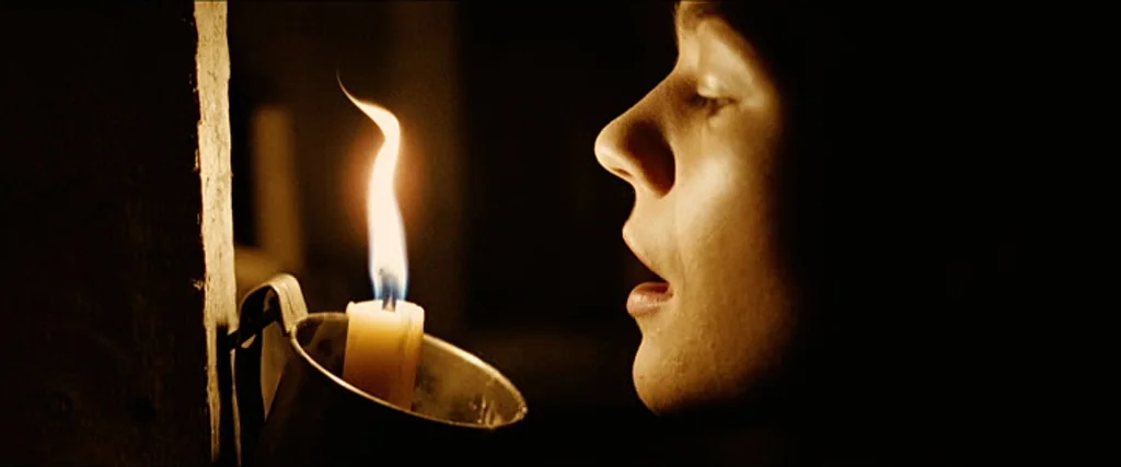 The Assassination Of Jesse James By The Coward Robert Ford (2007) movie still: closeup — A dark indoor space is lit solely by the warm glow of a…