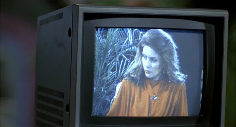 Videodrome (1983) movie still: closeup — A small black cathode-ray tube television displays a broadcast of a woman. The woman stands against a leafy…