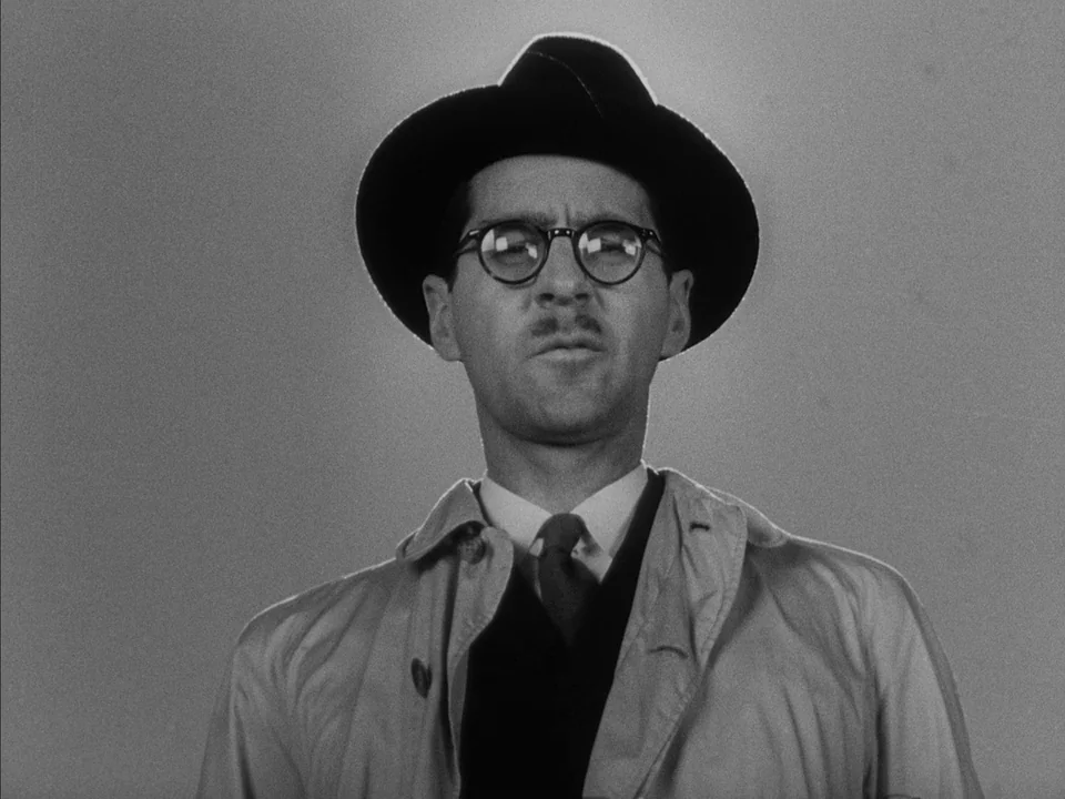 It Rains On Our Love (1946) movie still: closeup — The man stands against a uniform gray background in broad daylight. He wears a fedora and a…