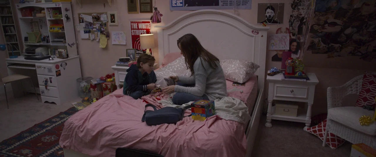 Room (2015) movie still: wide — A cluttered child's bedroom features pink bedding, white furniture, and posters on the walls. A woman and a young…