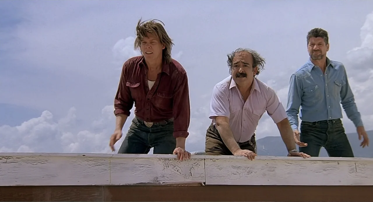 Tremors (1990) movie still: medium — Three men lean over the edge of a white wooden structure against a sky. They look downward with serious…