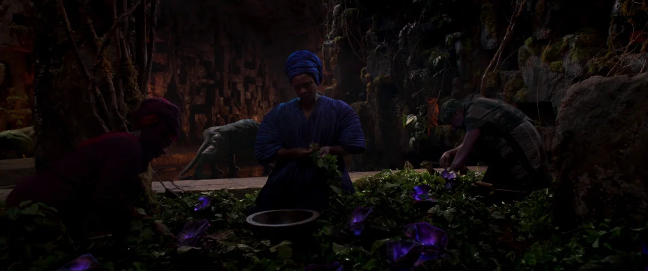 Black Panther (2018) movie still: wide — A dark subterranean grotto features mossy rock walls and glowing purple flora on floor. Three figures in…