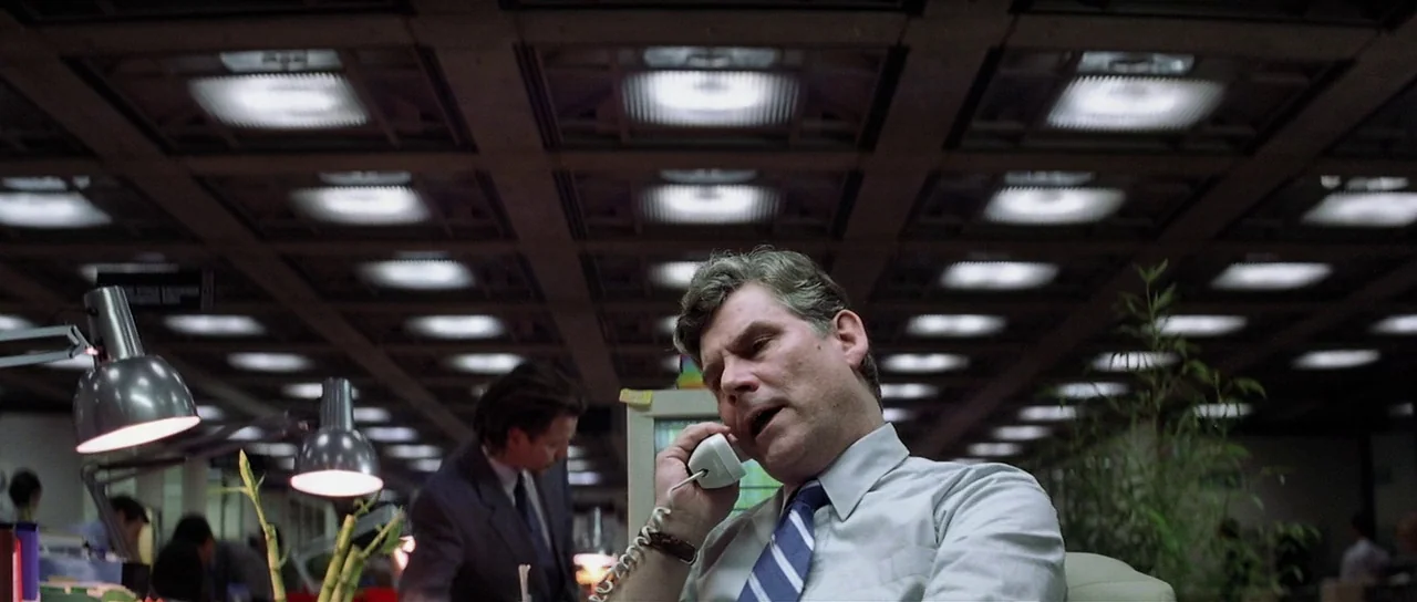 Spy Game (2001) movie still: medium — An open plan office features a dropped ceiling with modular fluorescent light fixtures. A man in a dress shirt…