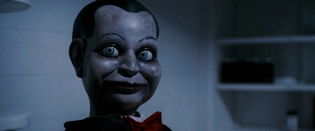 Dead Silence (2007) movie still: closeup — A dimly lit room with tiled walls and a partially visible shelf in background. A ventriloquist doll…