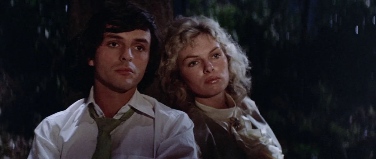 The Legend of the 7 Golden Vampires (1974) movie still: medium — A man and woman sit closely together outside amidst dark foliage during a…