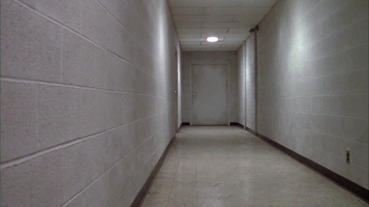 Day of the Dead (1985) movie still: establishing — A long, sterile hospital corridor features pale white cinder block walls and tiled flooring. A…