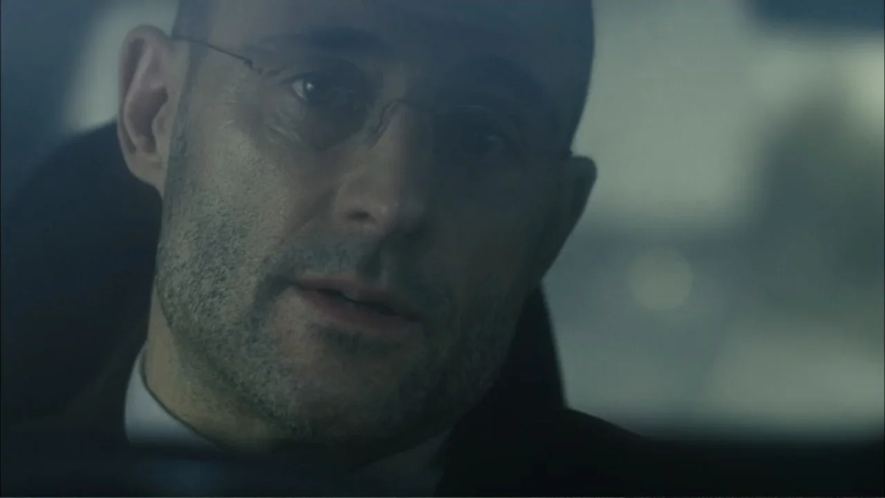 Before I Go to Sleep (2014) movie still: closeup — A close view inside a vehicle with a dark interior setting. A middle-aged man with a shaved head…