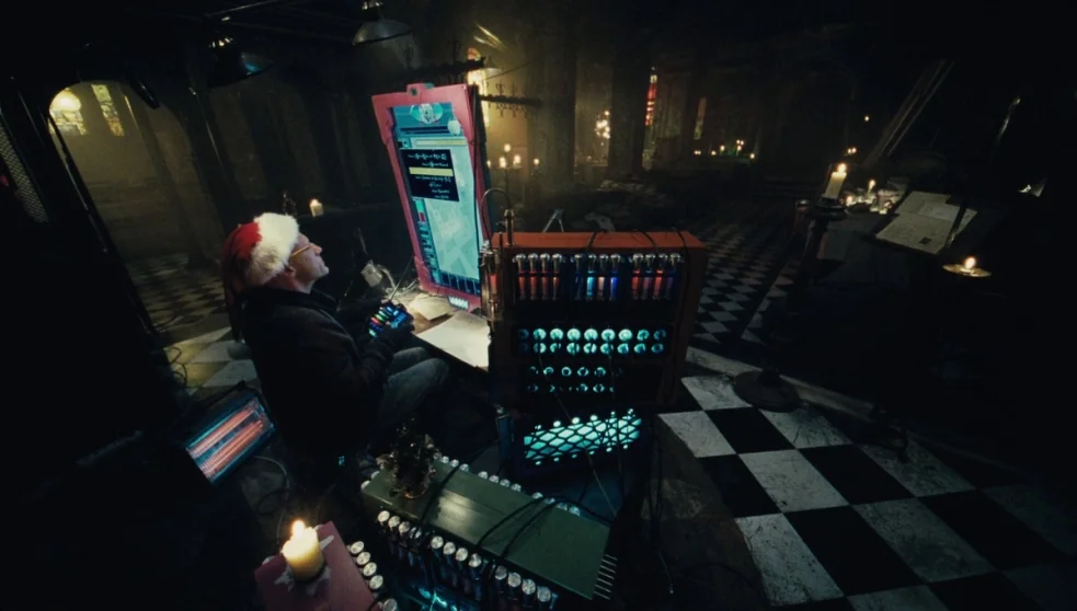 The Zero Theorem (2013) movie still: medium — A stone interior with black and white checkered tile flooring lit by many candles. An older man…