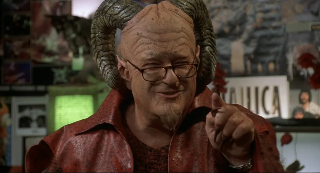 Little Nicky (2000) movie still: closeup — A man with large curved prosthetic horns stands inside a crowded record store. He points his finger at…