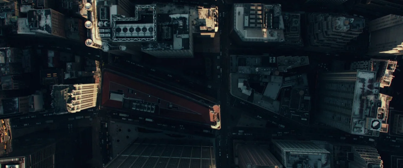 John Wick (2014) movie still: establishing — An overhead aerial view of a dense urban grid of skyscrapers and streets. The distinctive triangular…