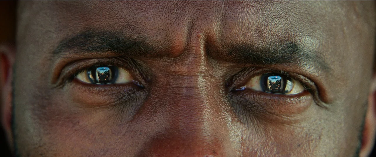 The Harder They Fall (2021) movie still: closeup — An extreme close-up of a man's eyes and the bridge of his nose. Tiny reflections of urban traffic…
