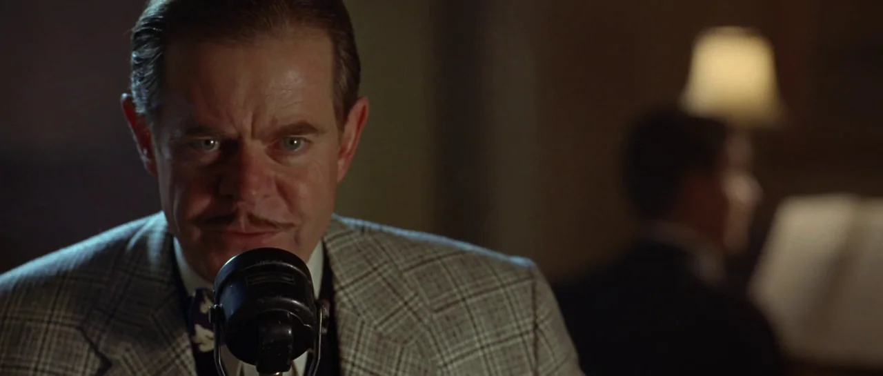 Seabiscuit (2003) movie still: closeup — A dimly lit room with a man positioned close to a vintage broadcast microphone. He stands in the foreground…