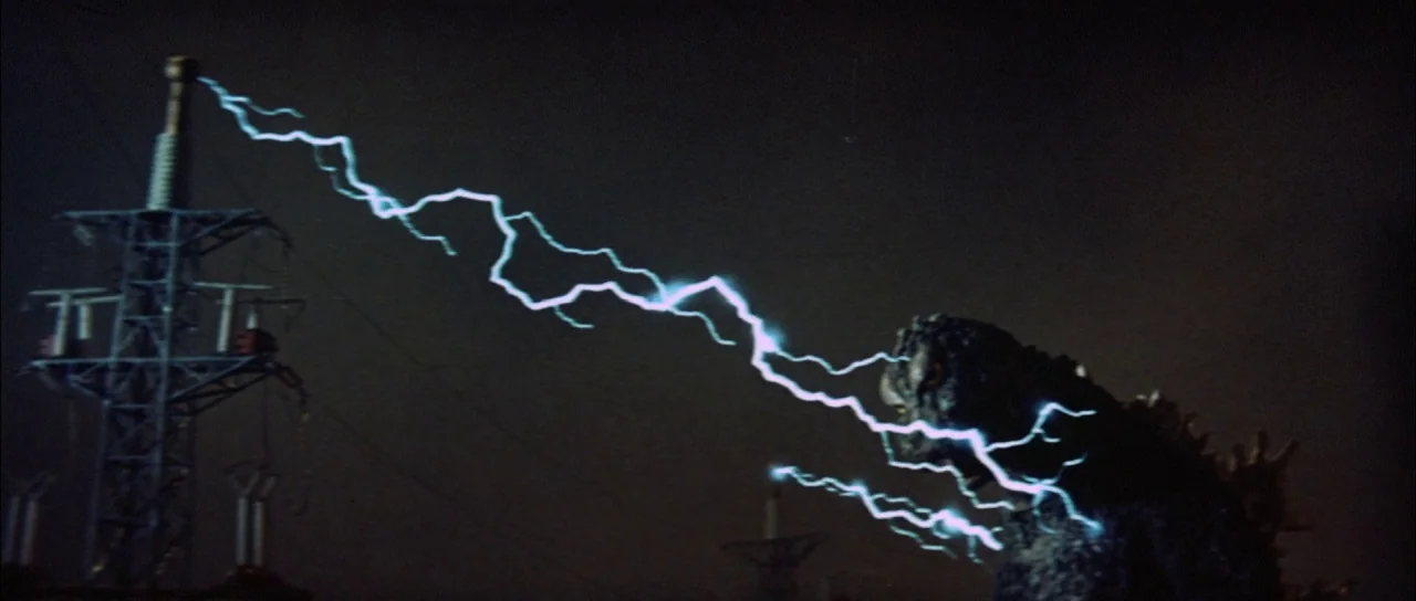 Mothra Vs Godzilla (1964) movie still: wide — A dark night landscape shows a tall metal transmission tower against the sky. A creature absorbs…