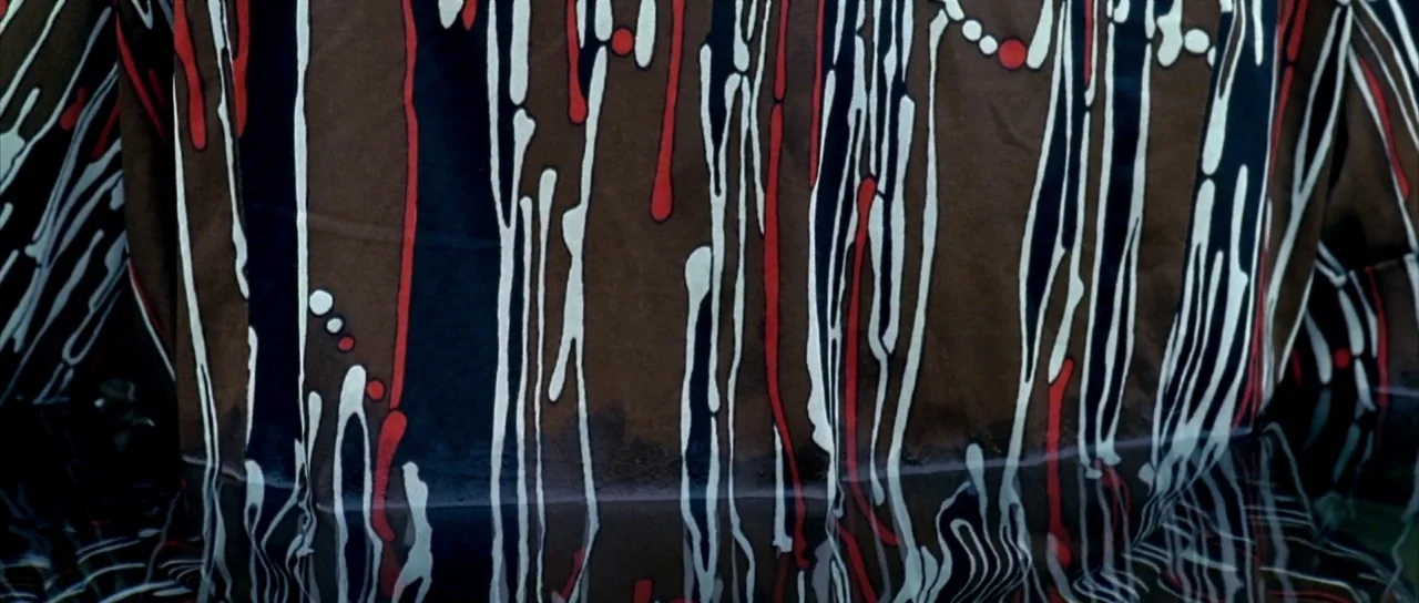 Sympathy for Mr. Vengeance (2002) movie still: closeup — A piece of brown fabric with a white and red vertical drip pattern is submerged. The fabric…
