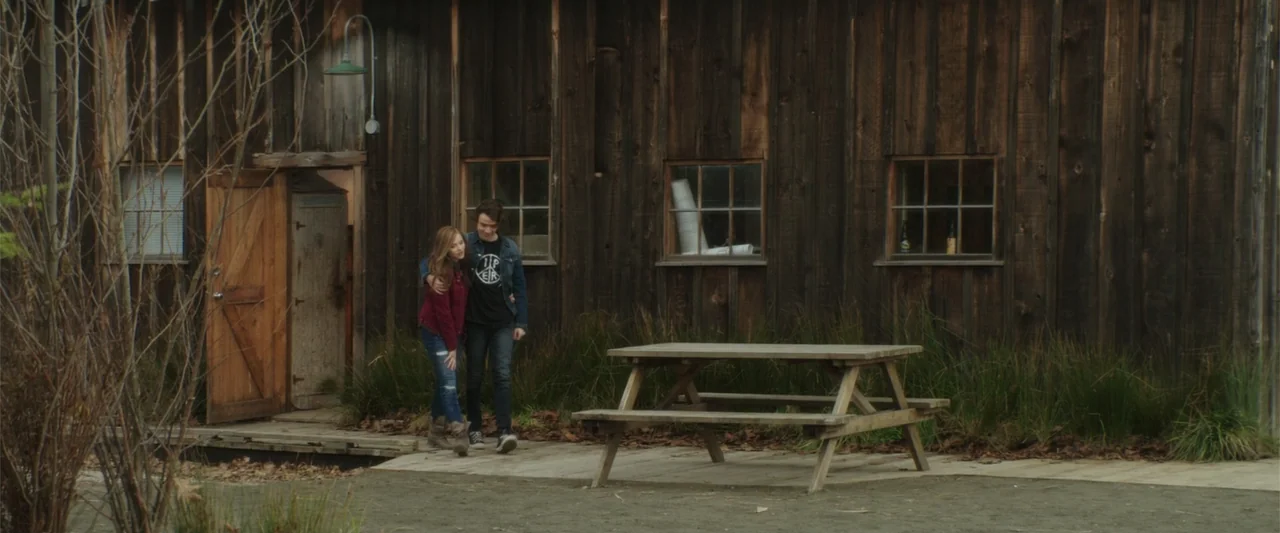 If I Stay (2014) movie still: fullbody — A rustic wooden barn exterior features horizontal planks and small multi-paned windows. A young couple…