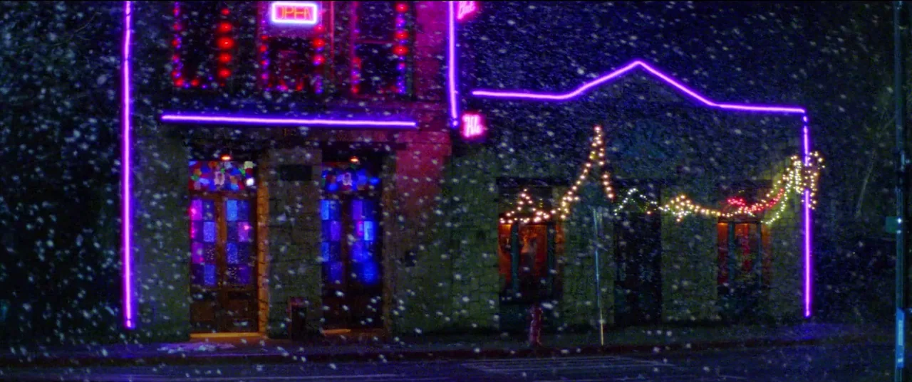 Christmas Bloody Christmas (2022) movie still: establishing — A stone building at night is decorated with vibrant purple neon borders and string…
