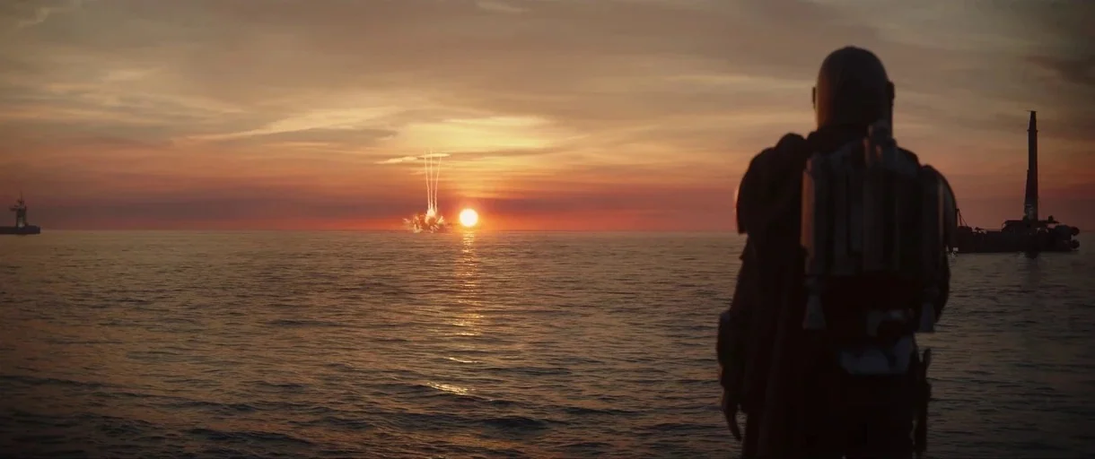 The Mandalorian (2019) movie still: wide — A vast ocean reflects the orange glow of a setting sun on the horizon. A armored figure in silhouette…